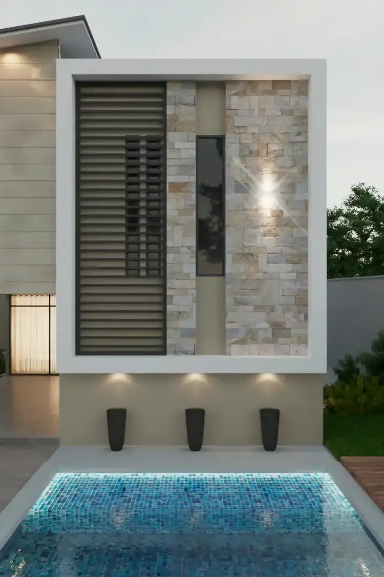 Vista de la fachada moderna de una casa de dos pisos diseñada por Edson Sánchez Arquitecto en Barranquilla, destacando una pared de piedra natural, lamas de madera verticales, iluminación de acento y una piscina de mosaicos azules con deck de madera al atardecer